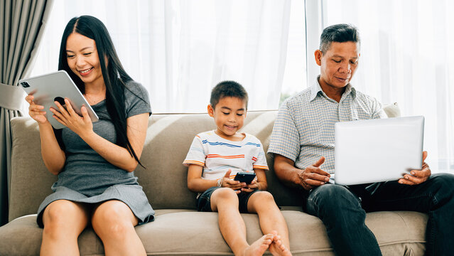 An Asian family engrossed in gadgets at home neglecting togetherness. Parents and kids addicted to devices showcase the impact of internet dependency on family bonding.