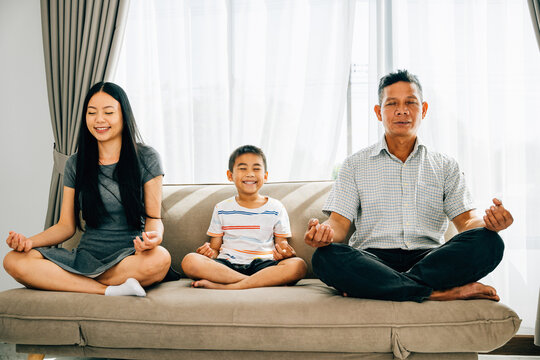 A tranquil scene, a young family meditates in lotus posture on a sofa promoting relaxation and mindfulness. An embodiment of peacefulness and family unity at home.