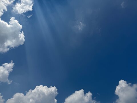 Sun rays breaking through white cumulus clouds in deep blue sky