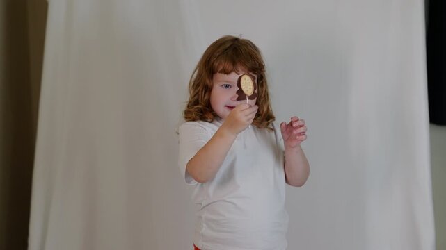 A little girl is holding a chocolate dessert on a stick and playing in the studio. The concept of childlike fun and a sweet dessert, with a cute child enjoying the treat.