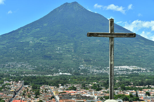 Cruz de piedra con vista hacia la ciudad de Antigua Guatemala, al centro el volc&aacute;n de Agua, espacio para texto al lado izquierdo.
