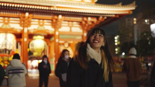 Young Asian woman travel traditional Japanese Sensoji Temple at night. Female tourist enjoy exploring culture sightseeing, winter tourism and local Japanese heritage experience on holiday vacation.