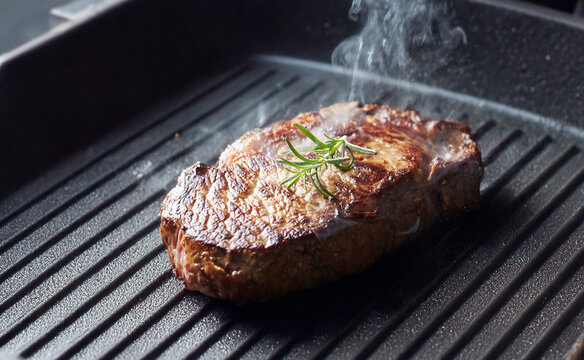 Juicy beef steak grilling on hot cast iron skillet with smoke and rosemary garnish
