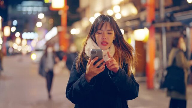Young Asian woman using smartphone navigation while travel traditional Japanese street at night. Female tourist exploring Japan cultural sightseeing, mobile map technology, tourism on holiday vacation