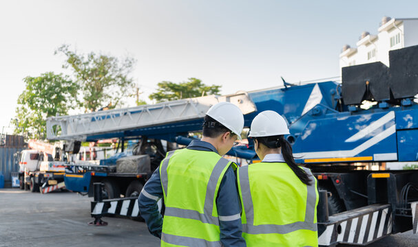 Medium lifting equipment inspection shot features male and female engineers wearing hard hats examining a blue mobile crane