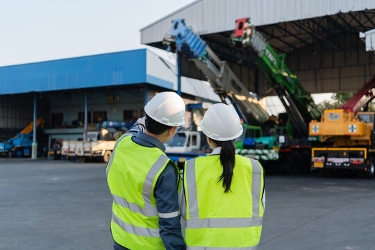 Telescopic crane boom undergoing preventive maintenance is visually inspected by two engineers wearing reflective vests