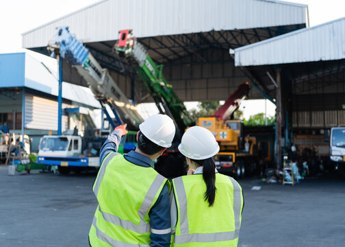 Crane boom lifting equipment inspection starts as two workers wearing hardhats observe the parked machinery hook block outside