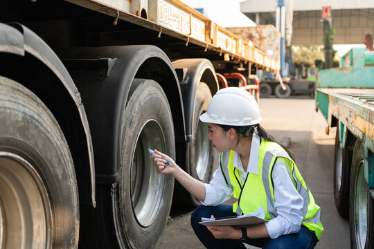 In a crane yard, preventive maintenance continues as one female engineer holds her clipboard to check heavy truck wheels