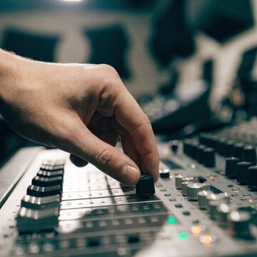Sound engineer hand adjusting knobs on mixing console; audio technician turning dials in recording studio; music producer mixing sound levels; dj controller interface details