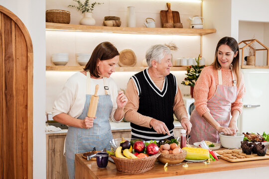 Happy multigenerational family preparing Christmas dinner together in a cozy home kitchen, cooking fresh food, smiling and sharing warm moments during the festive holiday season.