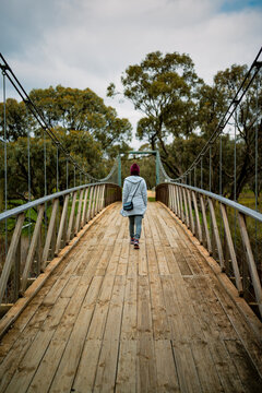Rear view of a woman walking across a timber suspension bridge surrounded by native woodland, Donald, Victoria, Australia