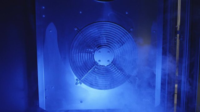 Industrial cooling fan operating in a blue-lit environment with cold vapor flowing through the ventilation system. Concept of thermal management, server cooling and data center infrastructure.