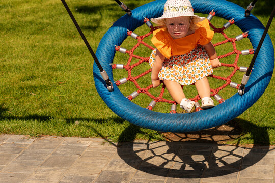 Toddler Girl Riding Blue Basket Swing in Sunhat