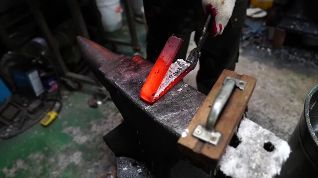Hand hammer striking a red hot blade blank on an anvil with borax flux scattered across the work surface