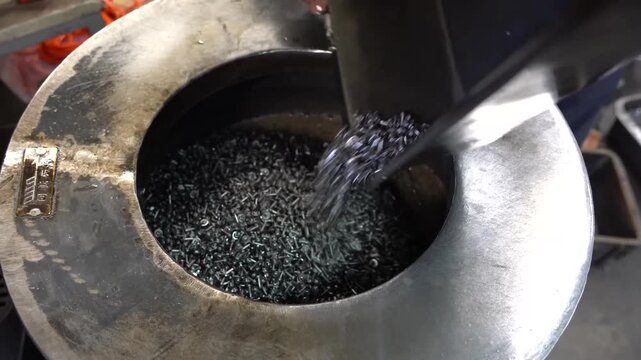 Raw metal chips pouring from a tray into a round hopper feeding a screw forming machine