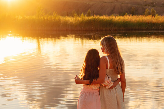 Mother And Daughter Watching Sunset Across Calm Water