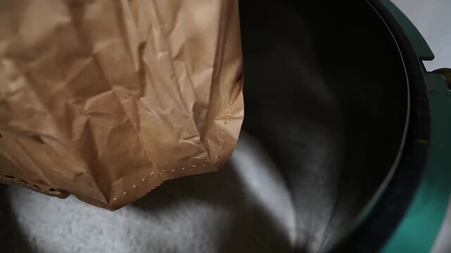 Factory worker pouring gray rubber granules from a paper bag into a machine hopper for eraser production