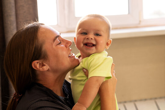 Laughing Mother Holds Cheerful Baby Son Near Window