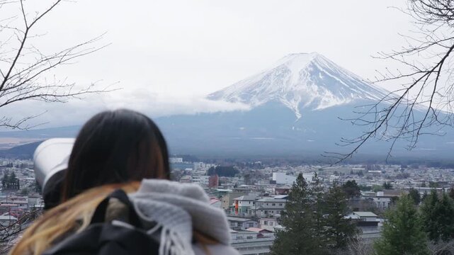 Asian woman tourist using observation telescope to view Mount Fuji in Japan, female traveler sightseeing scenic mountain landscape, winter vacation, Japanese tourism and famous travel destination