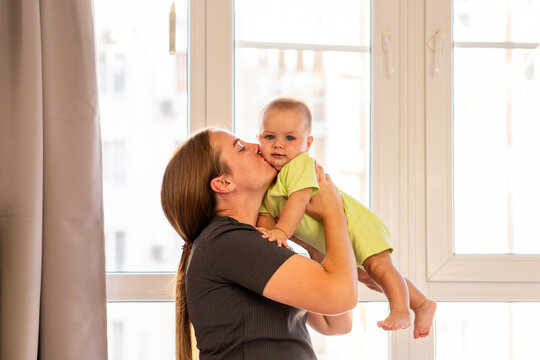 Mother Lifts Baby Boy And Kisses His Cheek Indoors