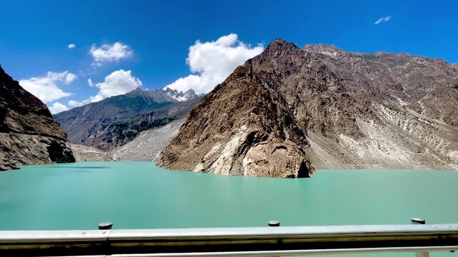 Attabad Lake in Hunza Valley, Gilgit Baltistan, Pakistan, featuring its striking turquoise water surrounded by steep, rugged mountains under a vivid blue sky and white clouds.