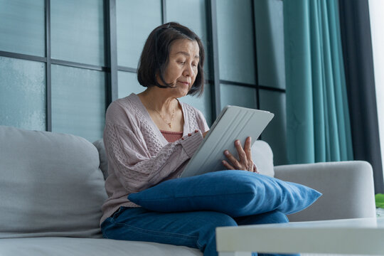 Asian mature woman using digital pen write note on tablet in living room