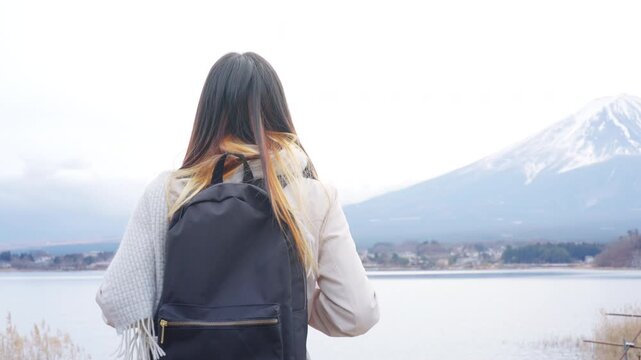 Young Asian woman tourist solo travel Mount Fuji and Lake Kawaguchi in Japan. Female traveler with backpack enjoy sightseeing scenic winter landscape, holiday vacation and Japanese landmark tourism