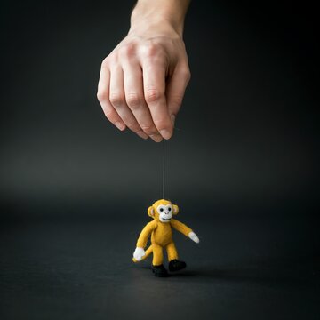 Hand holds a small toy monkey suspended by a string against a dark wall.