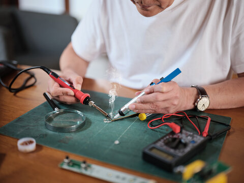 Close-up, man's hand repairs home electrical appliance, disassembling and soldering circuit board, focusing on precision detail, DIY fix tools, electronics component workshop hobby, expert handyman.