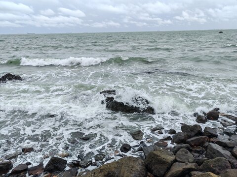 Rough ocean waves crashing against rocky shore under cloudy sky