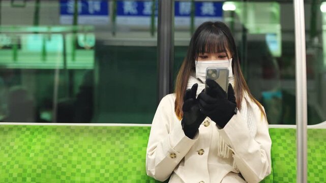 Asian woman wearing face mask using smartphone for online remote working or chatting while travel by train, public transportation passenger with mobile communication, railway commuter city lifestyle
