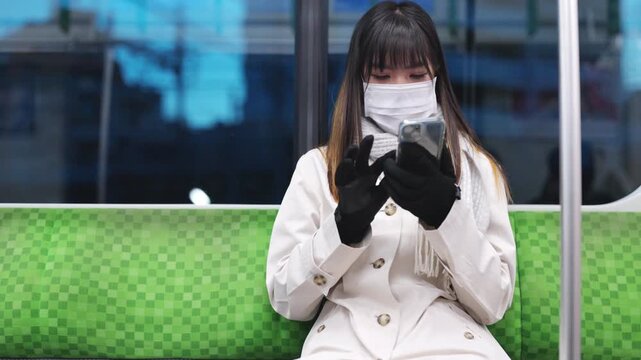Asian woman wearing face mask using smartphone for online remote working or chatting while travel by train, public transportation passenger with mobile communication, railway commuter city lifestyle