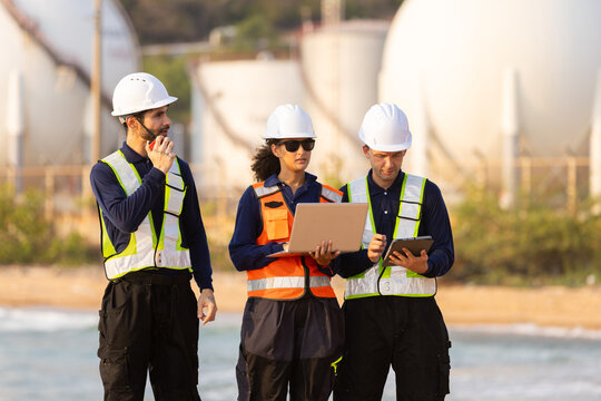 engineer team wearing safety helmet and vest reviewing document at industrial site near water storage tank facility working together with serious expression inspecting plant operations
