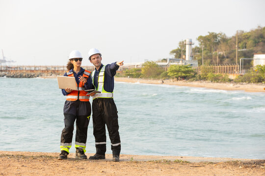 engineer team wearing safety helmet and vest reviewing document at industrial site near water storage tank facility working together with serious expression inspecting plant operations