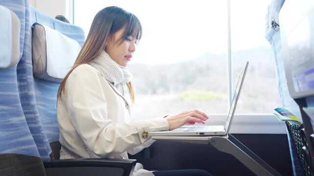 Asian businesswoman working on laptop while traveling by train, business travel, remote work and workation lifestyle. Female professional using computer during railway journey transportation commute