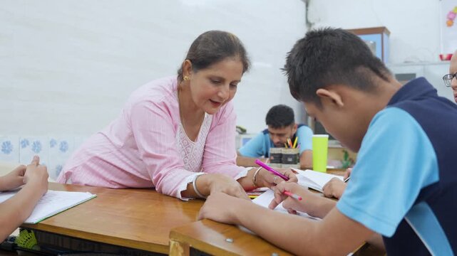 Caring female special education teacher providing one-on-one assistance to a student with learning disabilities, guiding his hand as he practices writing in a supportive classroom setting