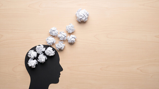 Black head silhouette with crumpled paper balls on wood background. Symbolizes brainstorming, creativity, mindset