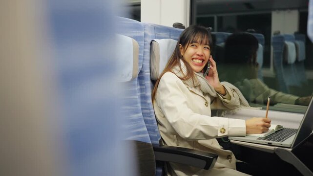 Asian businesswoman talking on smartphone and remote working on laptop while business travel by train. Female professional conference call mobile office during railway transportation commute workation