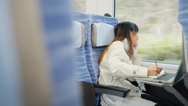 Asian businesswoman talking on smartphone and remote working on laptop while business travel by train. Female professional conference call mobile office during railway transportation commute workation