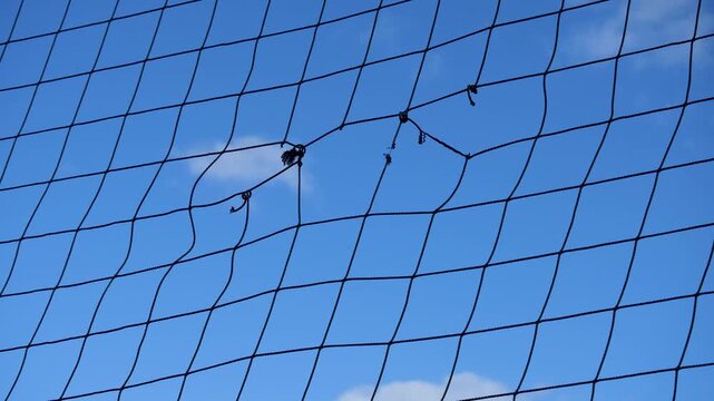 A torn black safety netting with frayed knots&nbsp;and worn mesh against a clear blue sky in Australia. Damaged sporting equipment, wear and tear, maintenance needs. Lack of maintenance at a public sports 