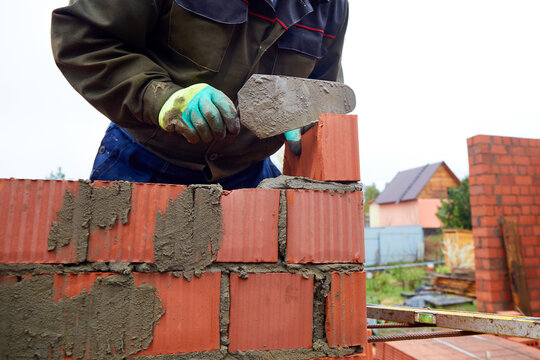 Close-up of a bricklayer building a red clay brick wall at a residential construction site.