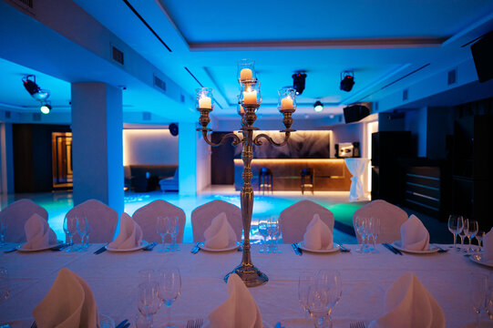Luxury indoor banquet table setting with candelabra and blue ambient lighting next to swimming pool