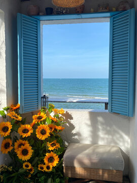 Blue window shutters open to ocean view with sunflowers and beach