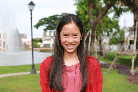 Happy young Asian girl smiling brightly for portrait in lush park, creating a cheerful, relaxed, and natural atmosphere.