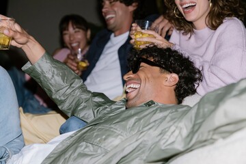 Obraz premium Group of diverse young adults laughing and holding drinks in a natural home setting with harsh flash lighting for social life and wellbeing