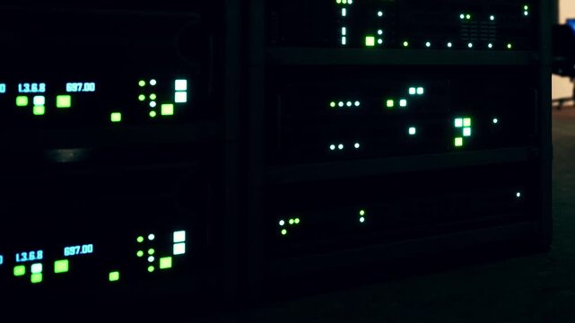 Lights on server racks blink and flash as data is processed. The setting is a data center during nighttime. The environment shows technology in use.