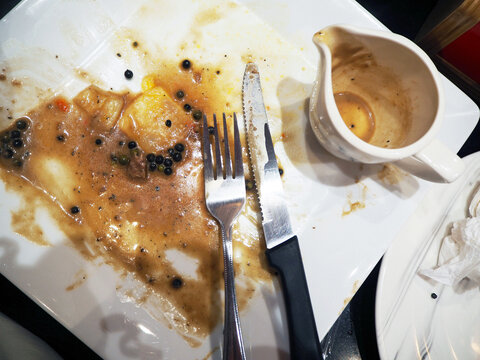 A dirty plate with leftover food, cutlery, and sauce, indicating the end of a meal