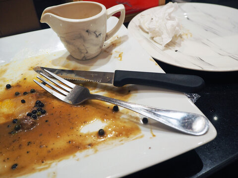 Messy plate after a delicious meal with fork, knife, and gravy boat on the side. The remnants of food and sauce are scattered across the plate, indicating a satisfying dining experience