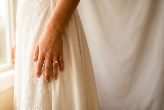 Bride displaying engagement ring on wedding dress with lace details