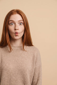 Young woman with surprised facial expression and red hair wearing cozy sweater